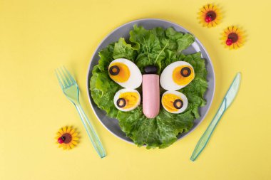 Kelebek, yumurta, sosis, siyah zeytin ve yeşil salata yapraklarından yapılmıştır. Çocuklar için sağlıklı bir kahvaltı fikri.