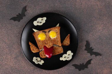 Sosisli, bıldırcın yumurtalı, siyah tabakta tatlı biberli ve peynirli Cadılar Bayramı canavarı sandviçi.