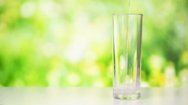 Masanın üzerindeki yeşil arka planı olan şeffaf bir bardağa saf su dökme görüntüsü. Stüdyoda çekilen su dökme görüntüleri..