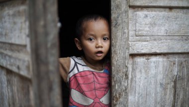 Ponorogo, Endonezya - 10 22 2021: Bir çocuk evinin sefil ahşap kapısını açar ve dışarıyı gözetler. Şok olmuş görünüyor..