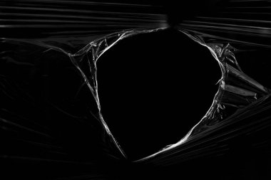 Siyah zemin üzerinde bir delik olan şeffaf plastik bir ambalaj. Kaplama ve efekt için gerçekçi yırtık plastik sargı dokusu. Yaratıcı ve dekoratif tasarım için buruşuk plastik desen.