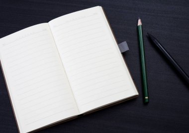 Üzerinde defter, kalem ve kalem olan siyah masa. Çalışma alanı olarak masanın üzerinde bir defter modeli var. ofis nesnesi siyah arkaplanda izole edildi.