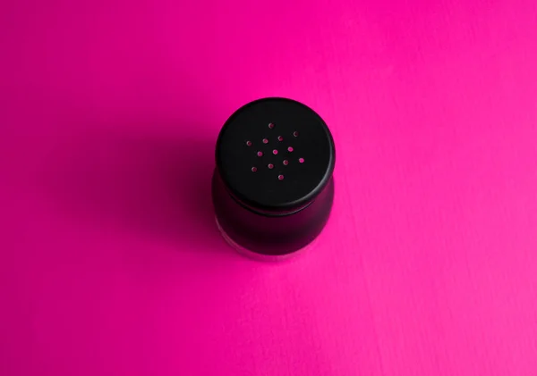salt or pepper shaker from the top point of view. seasoning powder container in black. food condiment shaker on pink background.