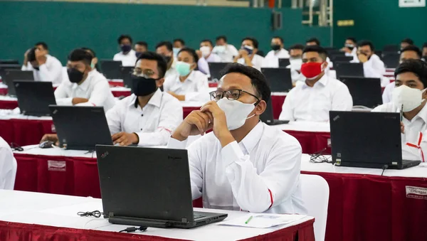 インドネシアのポノロゴ 2021年 パンデミックの公共イベントに参加する人々 白い上の服とダブルマスクを着てノートパソコンの前に座っています — ストック写真
