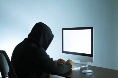 Siyah kapüşonlu kimliği belirsiz bir adam beyaz ekranın önünde oturuyor. İnternet tehditlerinin arka plan kampanyası için uygun bir portre.