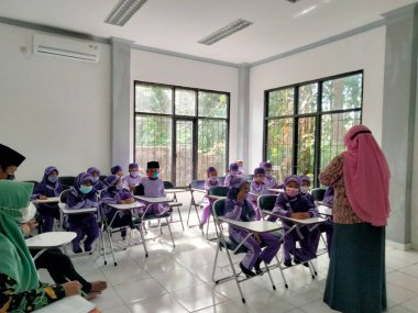 Ponorogo, Endonezya - 1227 2021: İlkokulda öğretmenlik. Öğrenciler ve öğretmenler salgın durumunda kendilerini korumak için maske takarlar..