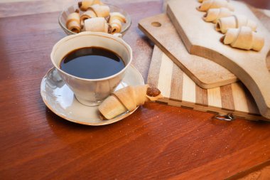 Elma reçelli kruvasan, üzerine pudra şekeri serpiştirilmiş ve tahta arka planda bir fincan kahve serpilmiş..