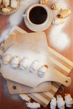 Elma reçelli kruvasan, üzerine pudra şekeri serpiştirilmiş ve tahta arka planda bir fincan kahve serpilmiş..