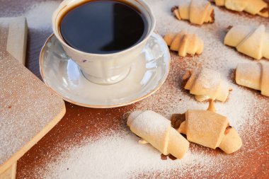 Elma reçelli kruvasan, üzerine pudra şekeri serpiştirilmiş ve tahta arka planda bir fincan kahve serpilmiş..