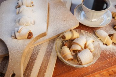 Elma reçelli kruvasan, üzerine pudra şekeri serpiştirilmiş ve tahta arka planda bir fincan kahve serpilmiş..