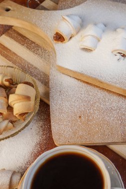 Elma reçelli kruvasan, üzerine pudra şekeri serpiştirilmiş ve tahta arka planda bir fincan kahve serpilmiş..