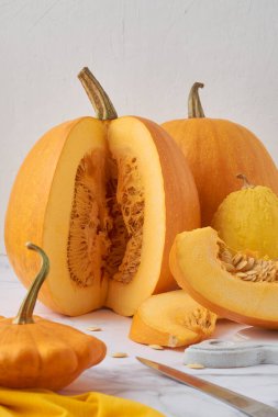 Beyaz arka planda, ışık masasında birkaç balkabağı. Bir balkabağı kesilir, yanında çekirdekli balkabağı parçaları olur. Hafif tonlama, dikey yönelim. 