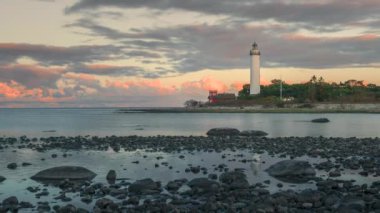İsveç deniz feneri Lange Erik 'in gün batımında Oeland' in kuzeyindeki adada, hareketli bulutlarla, önlerinde taştan bir sahille zaman atlaması.