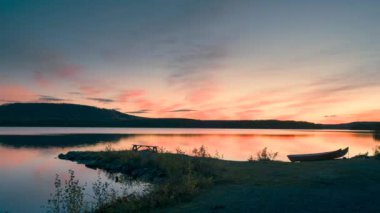 Günbatımında Stor-Skabram gölünde gün batımında Kuzey İsveç 'te Jokkkmokk yakınlarında, gökyüzünde renkli bulutlar hareket ederken, bankta oturan çift