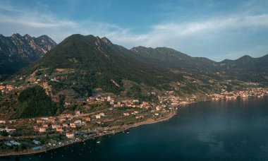 Iseo Gölü kıyısında öğleden sonra yukarıdan Marone köyü, dağlarla ve bulutlarla mavi gökyüzü, İtalya