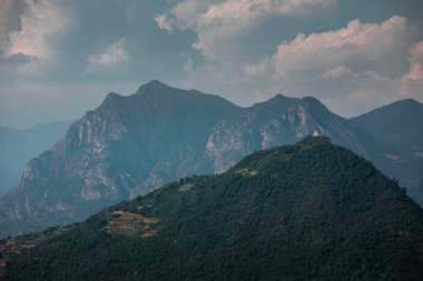 Iseo Gölü 'ndeki Monte Isola adasının zirvesinde Santuario della Madonna della Ceriola şapeli, arka planda dağlar, gökyüzünde bulutlar, İtalya