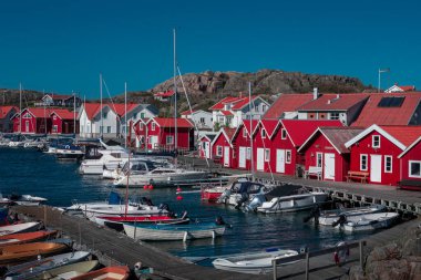 Red boathouses with boats at the coast under a sunny blue sky on the archipelago island of Tjoern in the west of Sweden