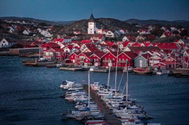 Red houses with church and boats in the harbor in the village of Skrhamn on the archipelago island of Tjoern on the west coast of Sweden during sunset from above