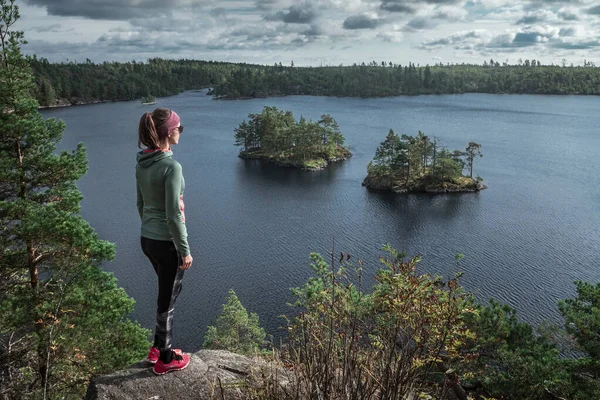 Woman standing in front of small islands in Lake Stensjoen in the Tyresta National Park in Sweden, during day with clouds in sky, from above