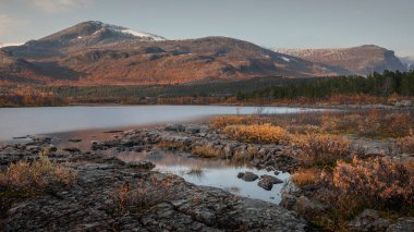 Landscape with forest at lake and mountains in Stora Sjoefallet National Park in autumn in Lapland in Sweden from above during sunset