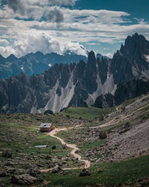 Rifugio Lavaredo dağ kulübesi gün boyunca Dolomite Alpleri 'nin önünde yukarıdan Three Peaks' te, turistler yürüyüş yolunda, bulutlar gökyüzünde
