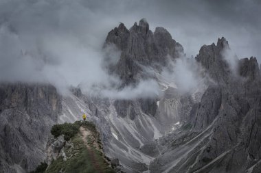 Güney Tyrol 'daki Dolomite Alpleri' nde dağın tepelerinin önündeki sarı ceketli adam dramatik bulutlu gökyüzü, Üç Tepe Doğa Rezervi, İtalya