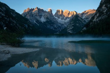 Toblach 'taki Lago di Landro Gölü' nün Alpenglow 'u. Dolomite Alpleri' nde güneş doğarken su yüzeyine yansıyan bir dağ zinciri. İtalya 'da sabah sisi.