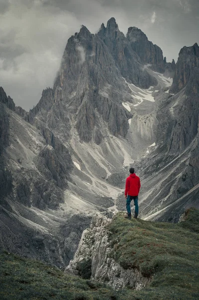 Man with red jacket in front of mountain peaks in the Dolomite Alps in South Tyrol with dramatic cloudy sky, Three Peaks Nature Reserve, Italy