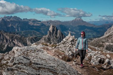 Dolomite Alpleri 'nde güneşli mavi gökyüzü gününde Passo di Falzarego' da Croda Negra Dağı zirvesine doğru yürüyüş yapan bir kadın.
