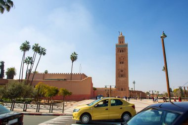  El Fnaa Camii 'nde panorama, kavşakta araba ve uzun palmiye ağaçları ve uzaktan tanınmayan insanlar - Afrika kışının sonunda güneşli bir gün.