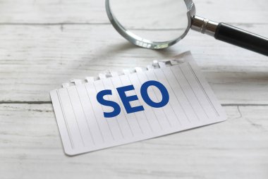 Selective focus of magnifying glass and paper written with SEO or Search Engine Optimization on white wooden backgorund.