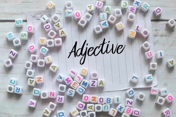 Top View Alphabet Beads Paper Written Adjective White Wooden Background — Stockfoto