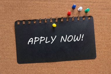 Renkli bir raptiye ve Apply Now ile yazılmış siyah bir kağıt! Bir mantar tahtada.