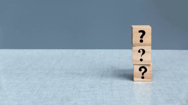 Gri arkaplandaki ahşap blok yığınındaki soru sembolleri.