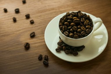 Beyaz fincanın seçici odağı, tahtadan arkaplana saçılmış kahve çekirdeği..