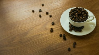 Beyaz fincanın seçici odağı kahve çekirdeği ile ahşap arka planda, fotokopi alanı ile dağılmış..