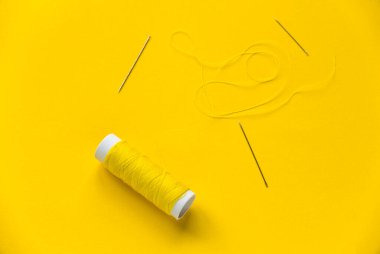 Sarı arka planda iğnesi olan sarı iplik makarası.