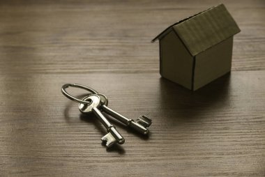 Ahşap masa üzerinde karton bir ev ve anahtar olan mülk veya gayrimenkul kavramı.