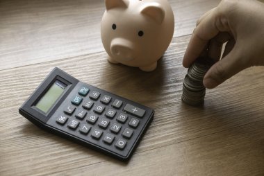 Business and finance concept with hand holding a stack of coins, piggy bank and calculator.