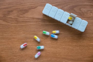 Top view of pill box with spilled pills on wooden table.