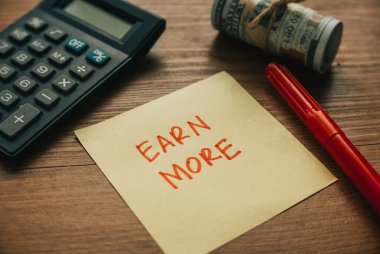 Hesap makinesinin seçici odak noktası, para kalemi ve kağıt Earn More ile yazıldı.