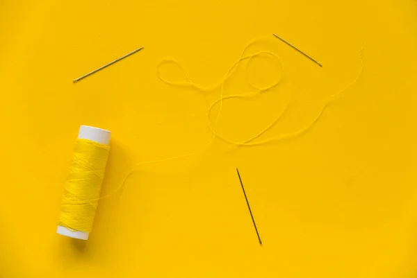 Yellow thread reel with a needle on yellow background