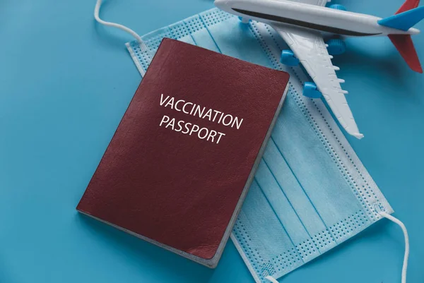 Concept of vaccination passport for travel with plane model and face mask on blue background.