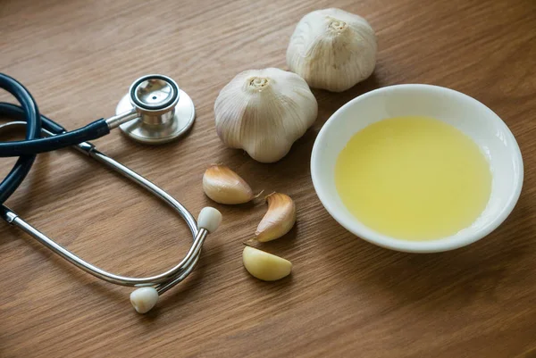 Selective focus of garlic ,garlic oil and stethoscope on wooden background.