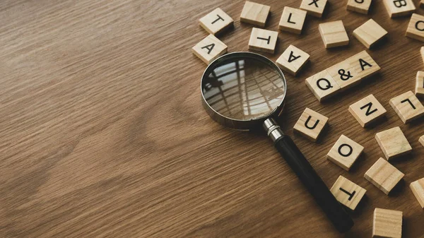 Q&A or questions and answers concept .Selective focus of wooden alphabet and magnifying glass on wooden background with copy space.