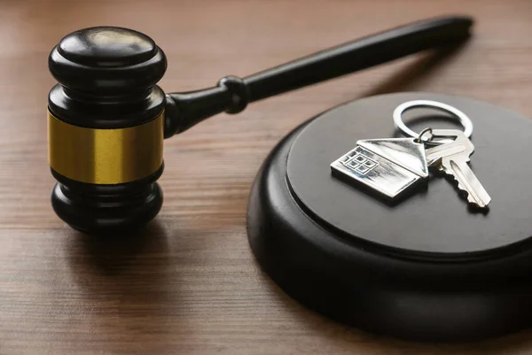 Real estate law and house auction concept. Selective focus of key with house keychain and gavel on wooden background.
