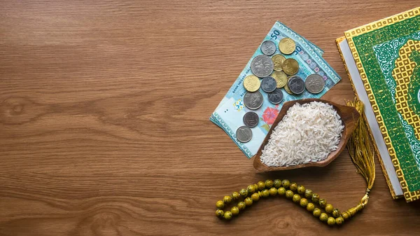 Concept of zakat in Islam religion. Top view of money, rice, Koran and prayer beads on wooden background with copy space.