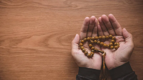 A hand holding prayer beads on wooden table with copy space.