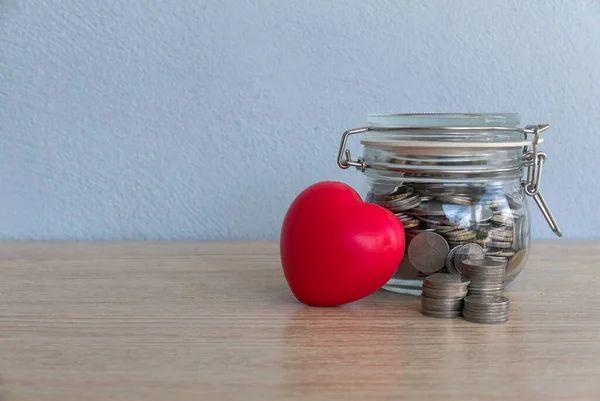A stack of coins,a jar of coins and red heart love on table with copy space.