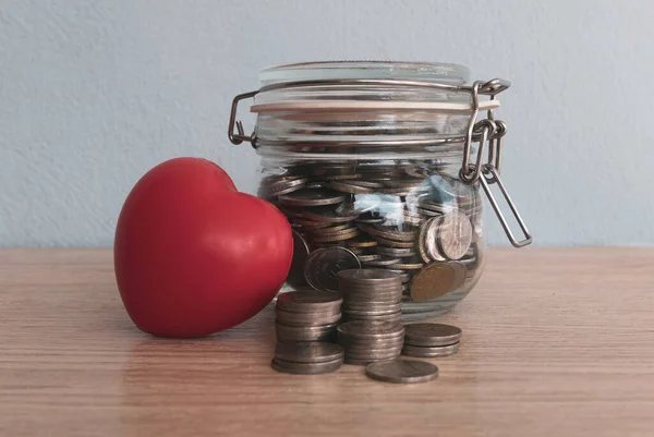 A stack of coins,a jar of coins and red heart love on table.